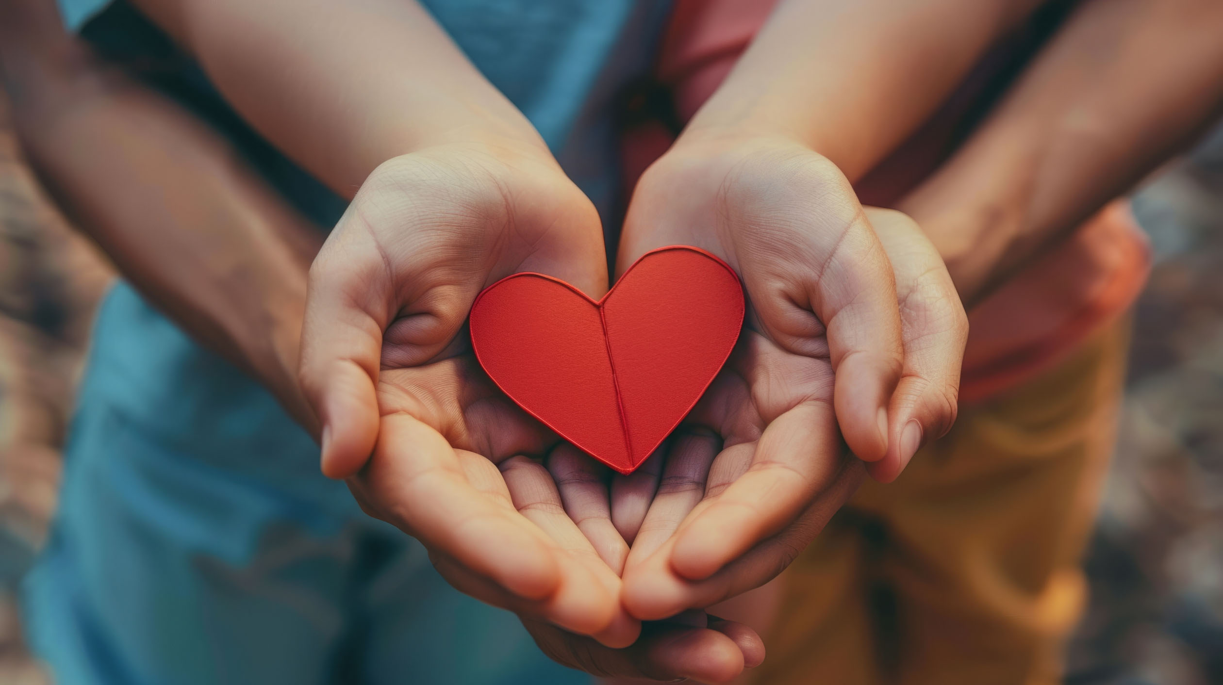 zwei Hand-Paare liegen ineinander und tragen ein kleines rotes Herz aus Pappe